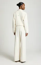 Pantalón sastrero de pierna ancha y tiro medio color marfil, confeccionado en algodón, con trabillas para cinturón, pliegues delanteros, bolsillos laterales y cierre frontal con cremallera y corchete.