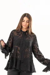 Blusa negra de tejido semitransparente con diseño floral en relieve, cuello alto con lazo frontal y mangas largas con volados en los puños.