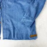 Sobrecamisa celeste de pana con cuello clásico, cierre frontal con botones a tono, dos bolsillos de parche con solapa abotonada en el pecho y mangas largas con puños abotonados.