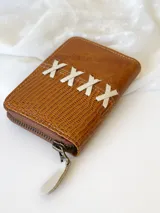 Billetera pequeña de cuero color camel con cierre metálico y diseño de cruces blancas. Incluye monedero interno.