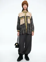 Camisa de corte oversize con diseño patchwork que combina paneles de tela a cuadros en tonos oscuros con paneles superiores de tela beige con estampado floral. Presenta cierre frontal con botones, cuello clásico y bolsillos delanteros con solapa.