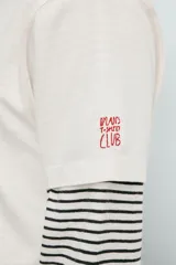 Camiseta de corte relajado color crudo, con cuello redondo y manga corta. Presenta un estampado frontal con una ilustración de Gizmo de la película Gremlins conduciendo un auto rojo y el texto 'Never ever feed them after midnight'.