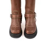 Bota de caña alta confeccionada en cuero vacuno engrasado color chocolate con efecto desgastado. Presenta bordados artesanales en la caña y el empeine, y cuenta con un sistema de correas con hebillas metálicas desmontables. Posee una suela track de goma negra de estilo robusto.