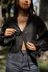 Blusa blanca de lino con mangas largas abullonadas, escote en V con lazo de ajuste frontal y detalles de puntilla en los bordes.