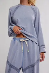 Conjunto de pijama de frisa lavada color celeste, compuesto por un buzo de calce amplio con escote redondo, mangas raglán abullonadas y puntilla aplicada sobre las costuras, y un pantalón de cintura elastizada con cordón, puños en los tobillos y detalles de puntilla en los paneles.