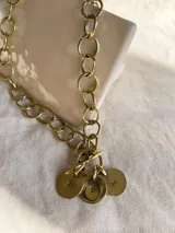 Cadena de eslabones grandes color bronce con cierre tipo toggle y tres dijes redondos con iniciales grabadas.