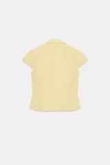 Top de cuello solapa y escote en pico, con manga corta y cierre frontal con botones. Presenta un diseño ajustado con detalles de frunces en el delantero.