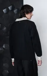 Sweater de punto negro con cuello polo en color crema, manga larga y diseño oversize. Presenta bordados en el frente con la inscripción 'Ravers', el número '90' y letras cursivas, con terminaciones en punto rib en puños y cuello.