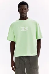 Remera de algodón verde menta de punto pesado, con corte holgado, hombros caídos, cuello redondo y estampa numérica frontal.