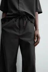 Pantalón de corte relajado confeccionado en tejido fluido con mezcla de lyocell. Presenta cintura elástica ajustable con cordón, bolsillos laterales y un bolsillo trasero de vivo con botón.