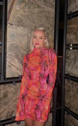 Vestido corto de microtul con estampado abstracto en tonos naranja y fucsia. Tiene cuello alto, mangas largas acampanadas y abertura lateral en la falda.