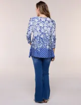 Blusa azul y blanca con estampado floral y geométrico, de calce suelto, con escote redondo, abertura tipo keyhole en el pecho, mangas tres cuartos y ruedo amplio con silueta evasé.