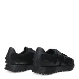 Championes urbanos New Balance modelo 327, color negro, confeccionados en una combinación de malla y material sintético. Presentan el logo 'N' característico en el lateral y una suela dentada que se extiende hacia el talón.