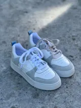 Zapatillas urbanas blancas con detalles en gris, suela plana y cordones blancos.