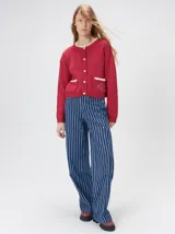 Cardigan de algodón grueso color rojo, con cuello redondo, cierre frontal de botones grandes y bolsillos cuadrados en el frente. Presenta detalles de pelo sintético en el cuello y los bolsillos, y logo bordado en uno de los bolsillos.