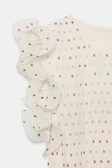 Top de cuello redondo y sin mangas, con volantes en los hombros. Presenta un estampado de lunares pequeños sobre fondo claro, con textura plisada y cierre de botón en la espalda.