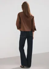 Camisa de algodón color marrón, de diseño recto, con cuello camisero, manga larga con puños abotonados y cierre delantero con botones.