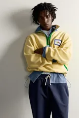 Sudadera polar de corte regular color amarillo, con cuello subido en tono azul, cierre frontal de cremallera verde y bolsillos con ribete verde. Incluye un parche gráfico de Fruit of the Loom en el pecho.