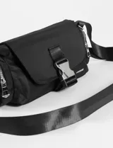 Bandolera de tela color verde militar, con tapa frontal y hebilla metálica. Cuenta con correa regulable y bolsillos laterales con cierre.