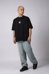 Remera de corte oversize confeccionada en algodón premium color crudo. Presenta un bordado frontal con la inscripción '90's' en color negro y un parche gráfico en la espalda con estética retro inspirada en los años 90.