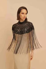 Capa de cuello alto negra, confeccionada con intrincados bordados de abalorios y cuentas que forman patrones ornamentales, adornada con largos flecos colgantes en todo el borde inferior.