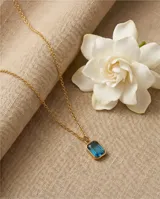 Collar de acero con baño de oro, compuesto por una cadena fina de eslabones y un dije rectangular con una circonia color celeste en el centro.
