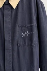 Mono oversize fit de algodón con estructura espiga en color azul marino, con cuello solapa en contraste de color tostado, manga larga, bolsillos de plastrón en el pecho con firma bordada, trabillas laterales en la cintura y cierre frontal con cremallera y botonadura oculta.