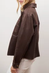 Chaqueta color camel con cuello camisero, cierre frontal con botones dorados, dos bolsillos de parche en el pecho y costuras decorativas en contraste.