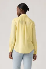 Camisa de lino color amarillo pastel, con bolsillos frontales con solapa, mangas largas remangadas y cierre frontal con botones.