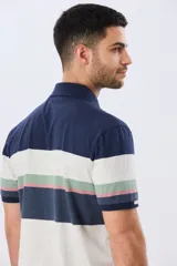 Remera polo de manga corta con diseño de franjas horizontales en tonos azul, beige, verde y terracota. Presenta cuello camisero con cierre frontal de dos botones y un pequeño bordado en el pecho.