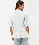 Remera overboxy de algodón color celeste, con cuello redondo, mangas cortas amplias y bajo asimétrico con aplicación de encaje blanco.