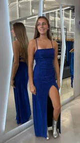 Vestido largo azul brillante con tirantes finos, escote recto, drapeado en la cintura y una abertura lateral alta en la falda. La espalda tiene un diseño de tiras cruzadas.