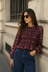 Blusa de manga larga con diseño de cuadros en tonos rojo y azul. Presenta un cuerpo con fruncido elástico (smock) que se ajusta a la silueta, cuello redondo y terminación con volado en la cintura.