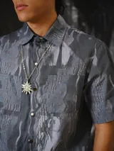 Camisa de manga corta con estampado abstracto en tonos grises, cuello clásico, bolsillos frontales aplicados y cierre frontal de botones a presión.