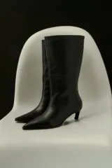 Bota de caña media confeccionada en cuero negro, con diseño de punta fina y taco bajo tipo kitten heel.