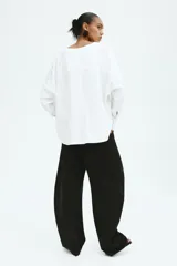 Blusa de algodón H&M Edition blanca con maxiescote en V, botones ocultos y canesú en la espalda. Presenta hombros caídos, mangas largas con puños abotonados y pinzas pronunciadas en la cintura que definen una silueta estructurada, con bajo asimétrico más largo en la espalda.