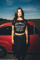 Remera tipo baby tee negra con ribetes rojos en cuello y mangas, y estampa frontal blanca con texto de marca y diseño de estilo vintage.