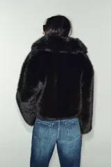 Abrigo corto de piel sintética en color negro, con cuello de solapa amplio, manga larga y cierre frontal con corchetes ocultos.