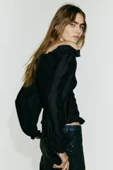 Blusa negra de viscosa con hombros descubiertos, cuerpo fruncido tipo nido de abeja y mangas largas con volumen y puños elásticos.