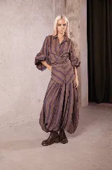 Camisa de lino con cuello solapa, cierre frontal con botones de coco, mangas abullonadas y puños elásticos. Presenta un diseño a rayas verticales en tonos tierra y violeta.