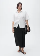 Camisa de manga corta con cuello camisero y cierre frontal de botones. Confeccionada en una mezcla de lino y algodón, presenta un diseño recto y minimalista.