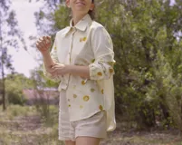 Camisa blanca con estampado de hojas en tonos beige y verde, cuello camisero, mangas largas con lazos en los puños y botones de madera.