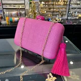 Clutch rectangular rígido de rafia sintética color fucsia, con cierre a tono y asa desmontable de cadena dorada para llevar al hombro.
