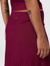 Conjunto de dos piezas confeccionado en tejido de punto acanalado color bordó. Incluye un top corto de cuello barco con mangas cortas y una pollera larga de corte acampanado.