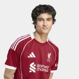 Camiseta de fútbol Adidas del Liverpool FC, modelo Home temporada 25/26, para hombre. Diseño color rojo oscuro con ribetes y detalles en blanco en cuello, mangas y hombros. Incluye el escudo del club y logos de patrocinadores.