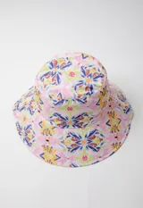 Gorro tipo bucket hat estampado con flores y hojas en tonos verde y celeste sobre fondo blanco. Es reversible.