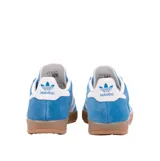 Championes Adidas Gazelle Indoor de gamuza azul con las icónicas tres rayas laterales en blanco. Presenta una suela de caucho color caramelo, talón blanco y detalles dorados con el nombre del modelo en el lateral.