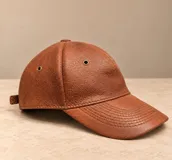 Gorro tipo visera de cuero marrón con ojales metálicos de ventilación y costuras decorativas en la visera.
