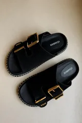 Sandalias de nobuck negro con dos tiras ajustables mediante hebillas doradas, suela plana con costura blanca decorativa en el borde y plantilla con el logo de la marca Vdamiani.