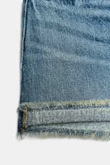 Shorts de jean de algodón, tiro alto, color azul claro desgastado. Presenta cinco bolsillos, cierre frontal con botón metálico y cremallera, y bajo desflecado con vuelta.